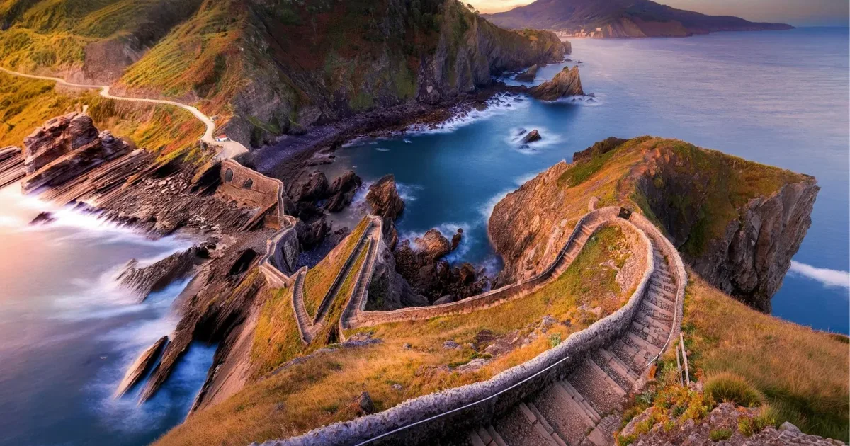 The switchback stone staircase at Gaztelugatxe at golden hour, looking down towards the cove and the Basque coast.