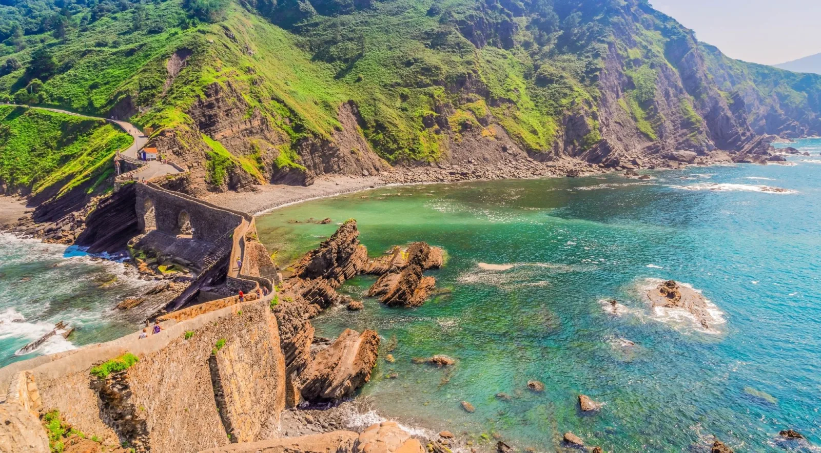 The Gaztelugatxe causeway and bridge above a turquoise cove backed by steep green cliffs
