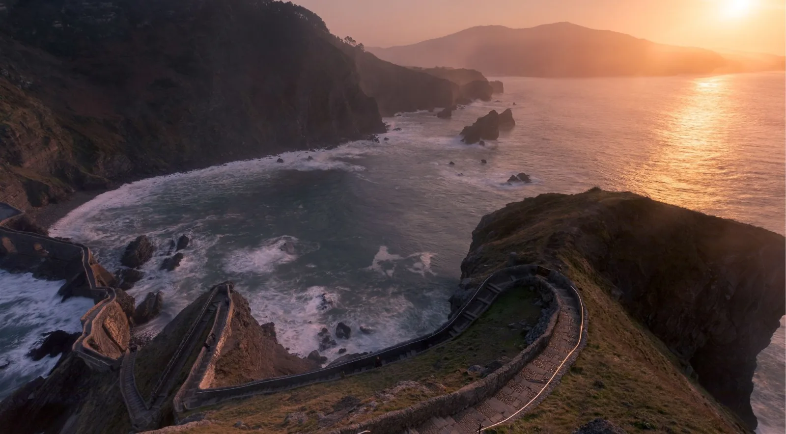 Sunset over the Gaztelugatxe cove seen from above, with the stone staircase curving along the ridge