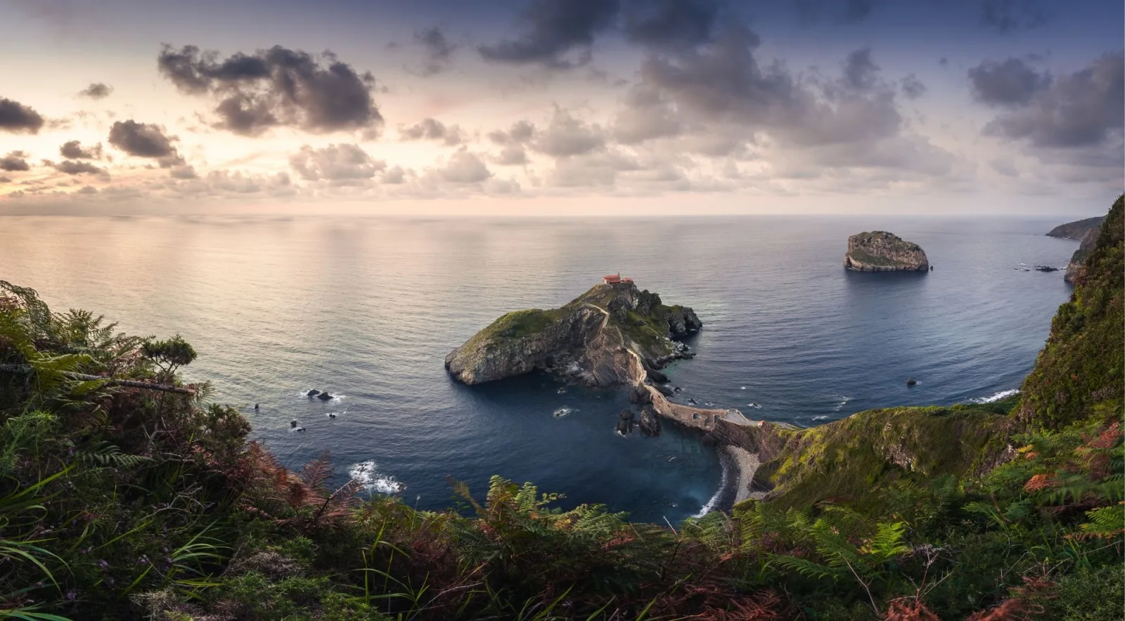 Wide panorama at sunset showing Gaztelugatxe, the causeway and the neighbouring islet of Aketx under broken cloud